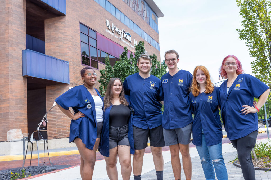 A group of six people wearing blue shirts stands outside a building, smiling and posing for the photo.
