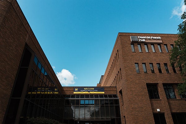 Exterior view of David M. French Hall, a brick university building with a blue sky and a banner welcoming students, faculty, and staff.