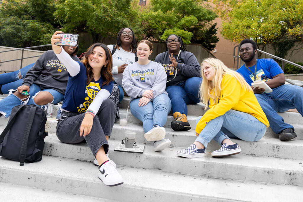 A group of people sitting on steps, with one person taking a selfie while others pose and interact.
