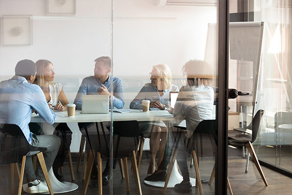 A group of people engaged in a discussion around a table in a glass-walled meeting room.