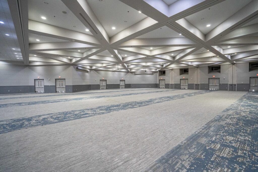 A spacious indoor venue with a patterned carpet, high ceiling, and multiple doors along the walls.