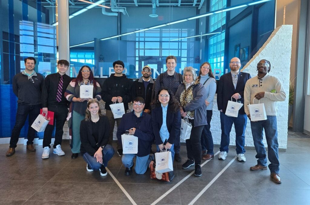 A group of people poses together indoors, each holding a bag, with a modern office setting in the background.