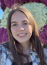 A person stands in front of a colorful floral backdrop, with a blurred face obscuring their identity.