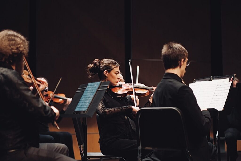 A group of musicians playing string instruments in a concert setting, with a focus on a person playing the violin.