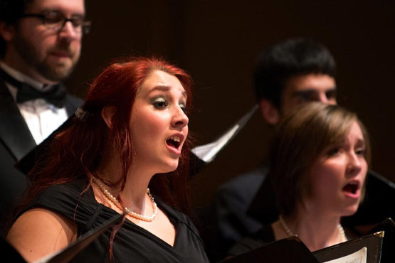 A group of singers performing in a choir, with one person prominently singing in the foreground.