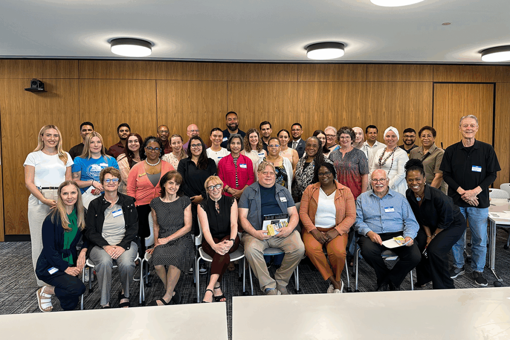 A large group of people poses for a photo in a conference room, with some seated and others standing, all smiling.