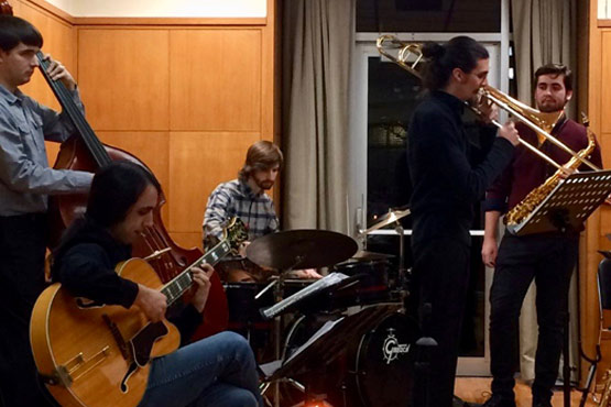 A group of five musicians performing together, featuring a guitarist, a trombonist, a bassist, and a drummer.