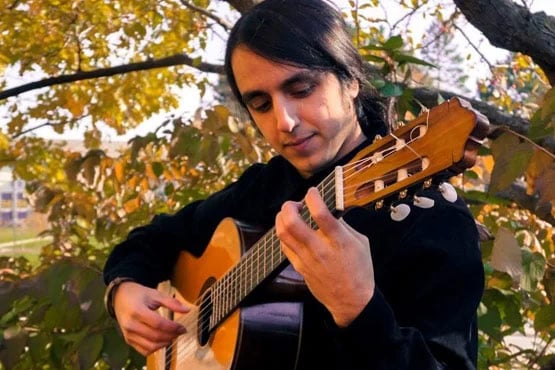 A person playing a guitar outdoors among autumn leaves.