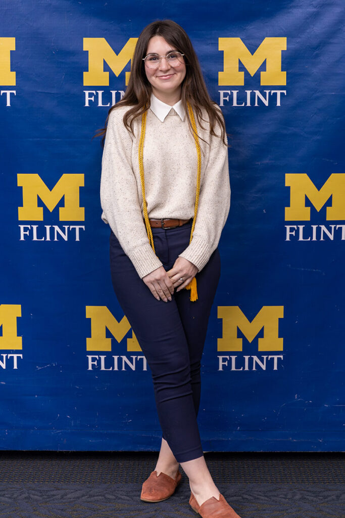 A person stands smiling in front of a blue backdrop with "M FLINT" in yellow letters.
