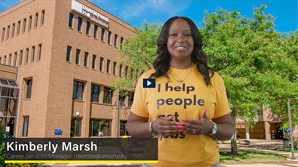 A person stands outside a building, wearing a yellow shirt that says "I help people get jobs," with a caption below.