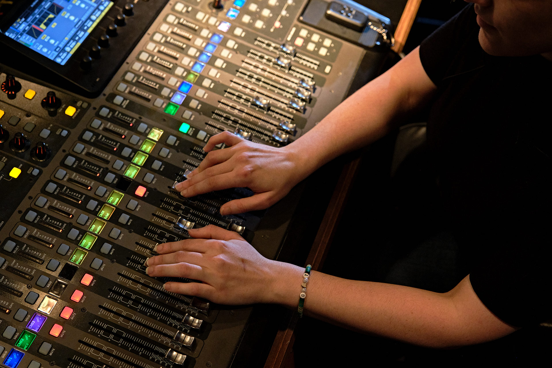 A person adjusts audio levels on a mixing console with multiple sliders and colorful buttons.