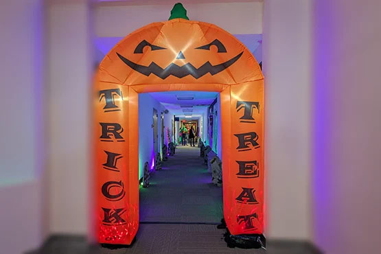 An inflatable archway shaped like a pumpkin with "TRICK" and "TREAT" written on it, leading into a brightly lit hallway.