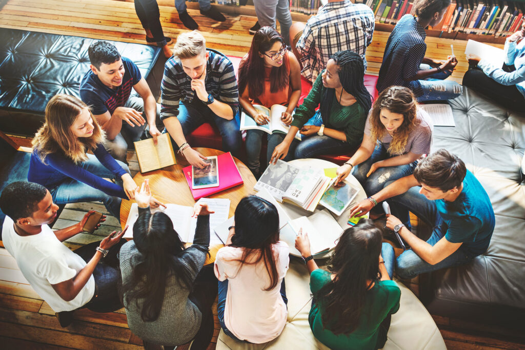 A group of students collaborates around a table, sharing books and notes in a cozy study space.