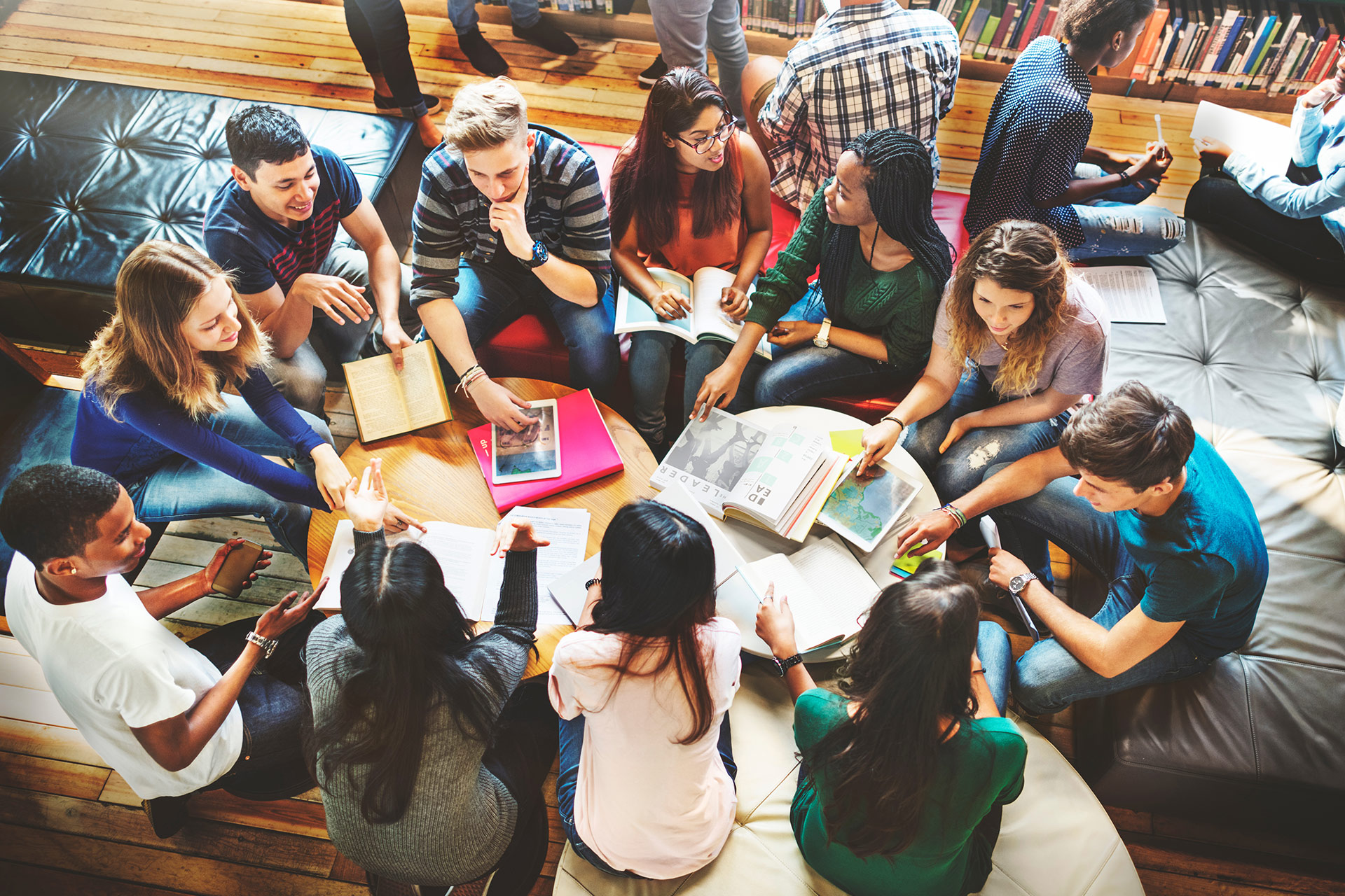 A group of students collaborates around a table, sharing books and notes in a cozy study space.