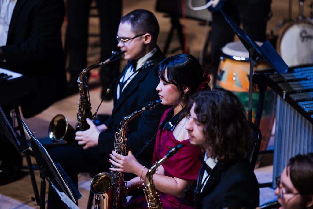 A group of musicians playing saxophones in a concert setting, with music stands in front of them.