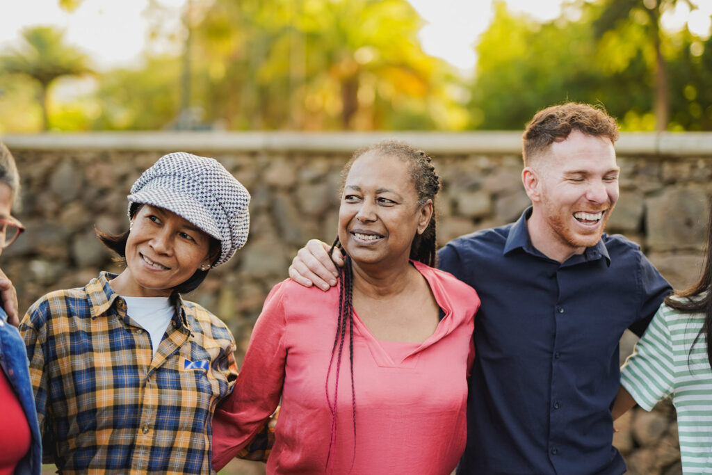 A group of four people stand together outdoors, smiling and interacting in a friendly manner.