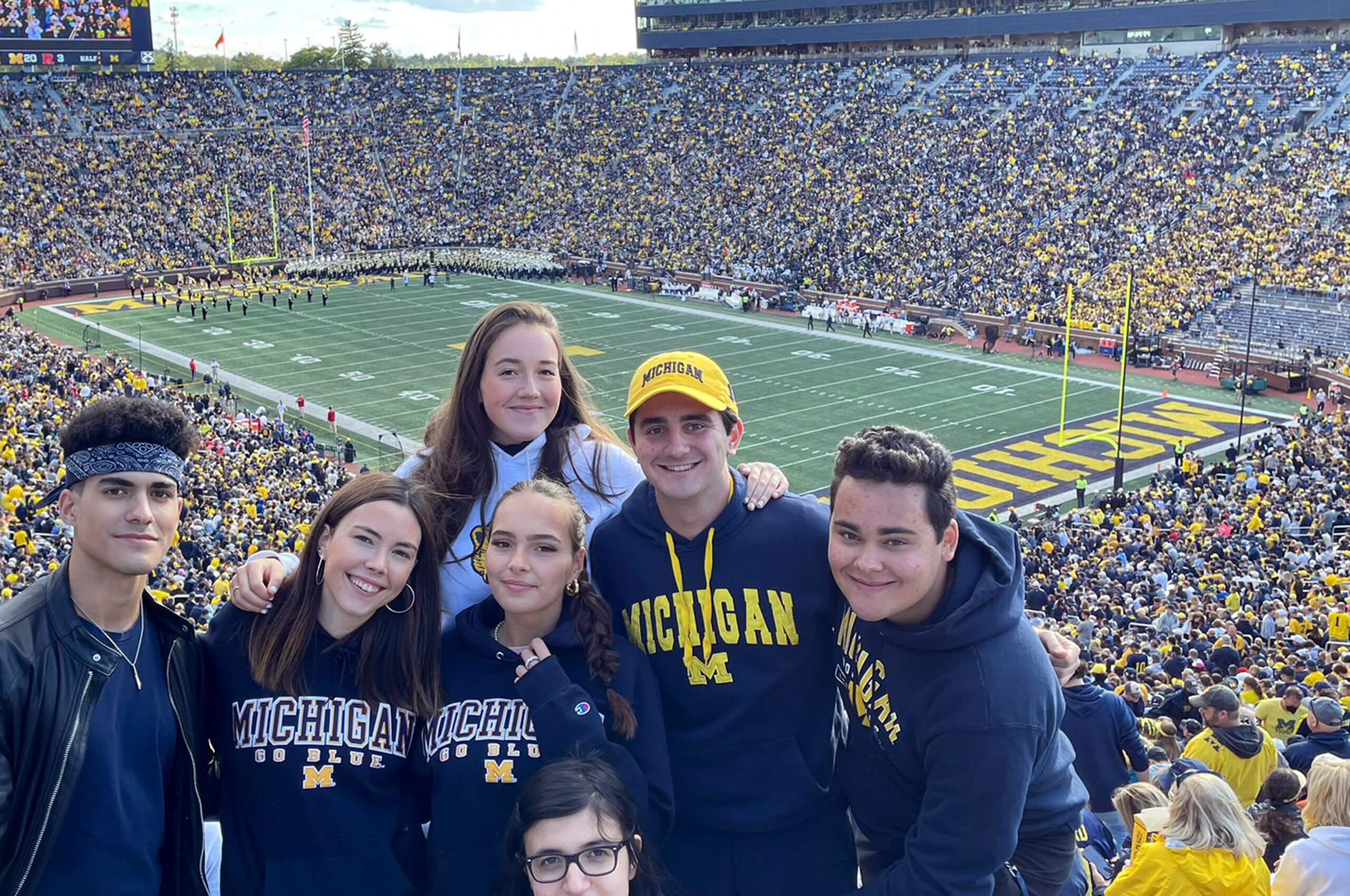 Six international students posing together in the stands at Michigan Stadium during a football game.