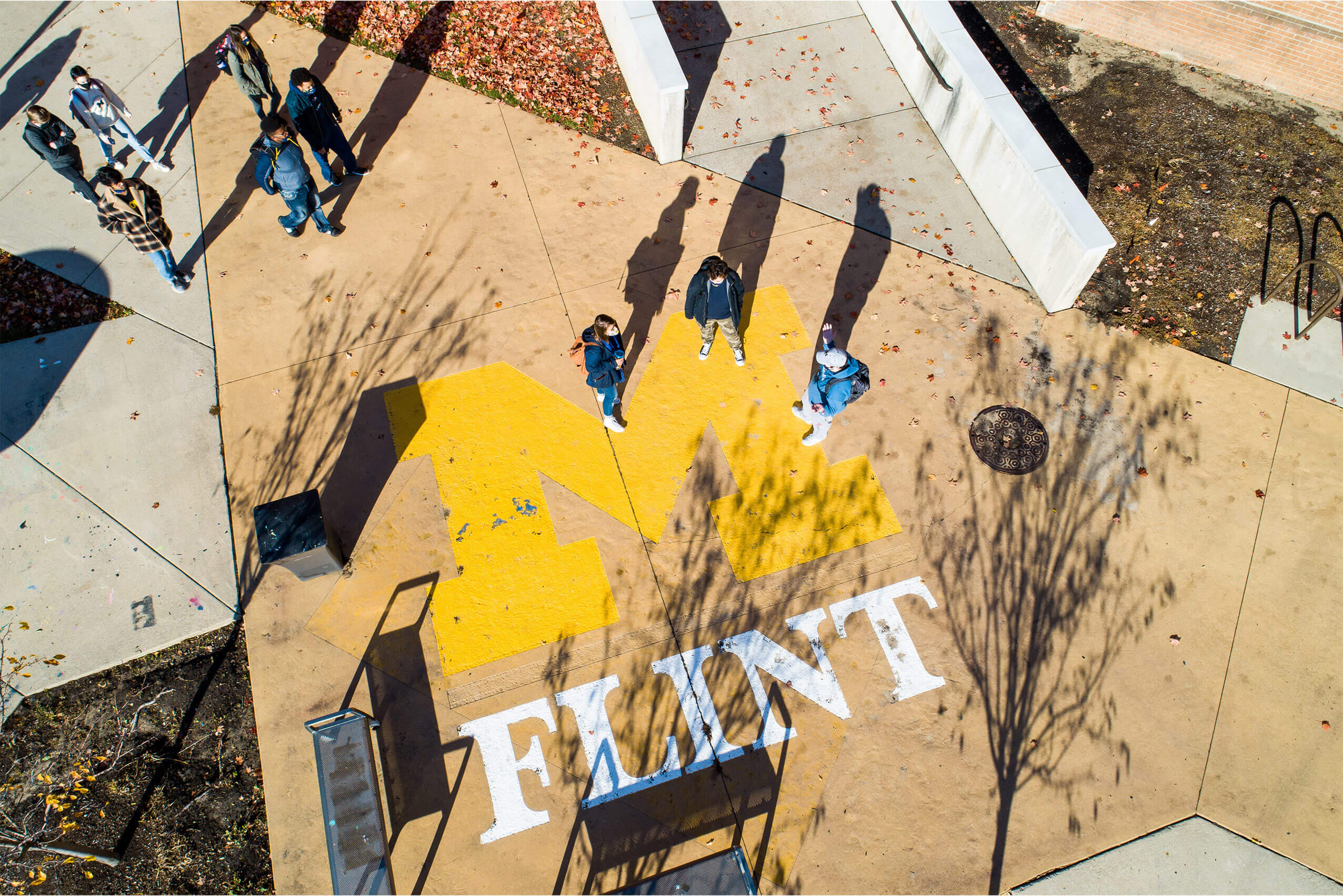 Aerial view of students walking across the maize block M and Flint logo painted on a campus walkway.
