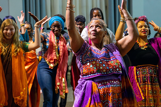 Students and staff in colorful traditional dress dancing with their arms raised at a UM-Flint cultural celebration.