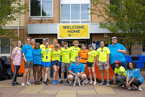 Student and staff move-in volunteers gathered under a Welcome Home banner outside the residence hall.