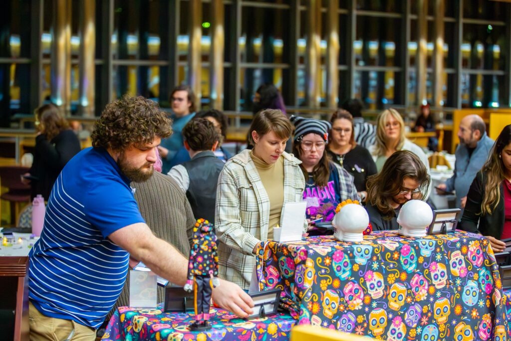 A group of people engaged in an activity at tables decorated with colorful, skull-patterned cloth, focusing on various items.