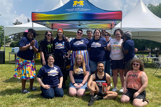 A group of people poses together in front of a colorful tent, smiling and celebrating at an outdoor event.