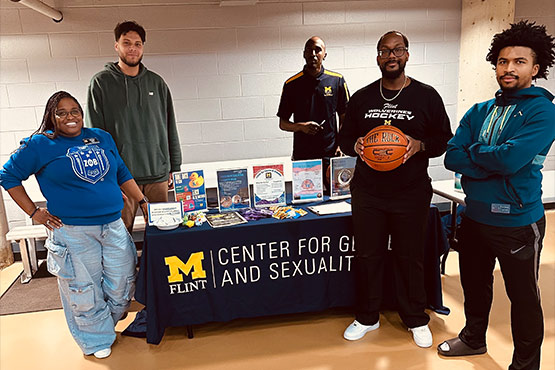 A group of five people stands behind a table displaying materials for the University of Michigan-Flint's Center for Gender and Sexuality.
