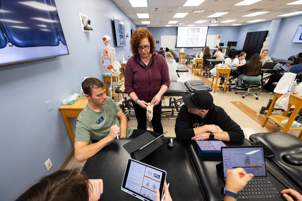 A physical therapy instructor uses a model of the foot to guide students during a hands-on anatomy lab.