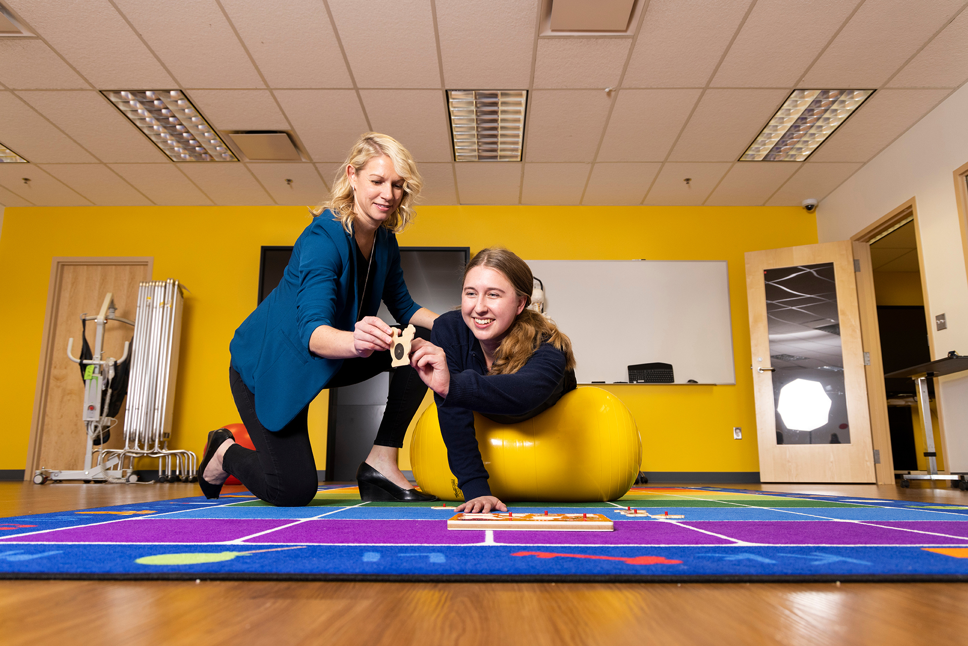 A UM-Flint occupational therapy student balances over an exercise ball while placing a wooden puzzle piece with guidance from an instructor.