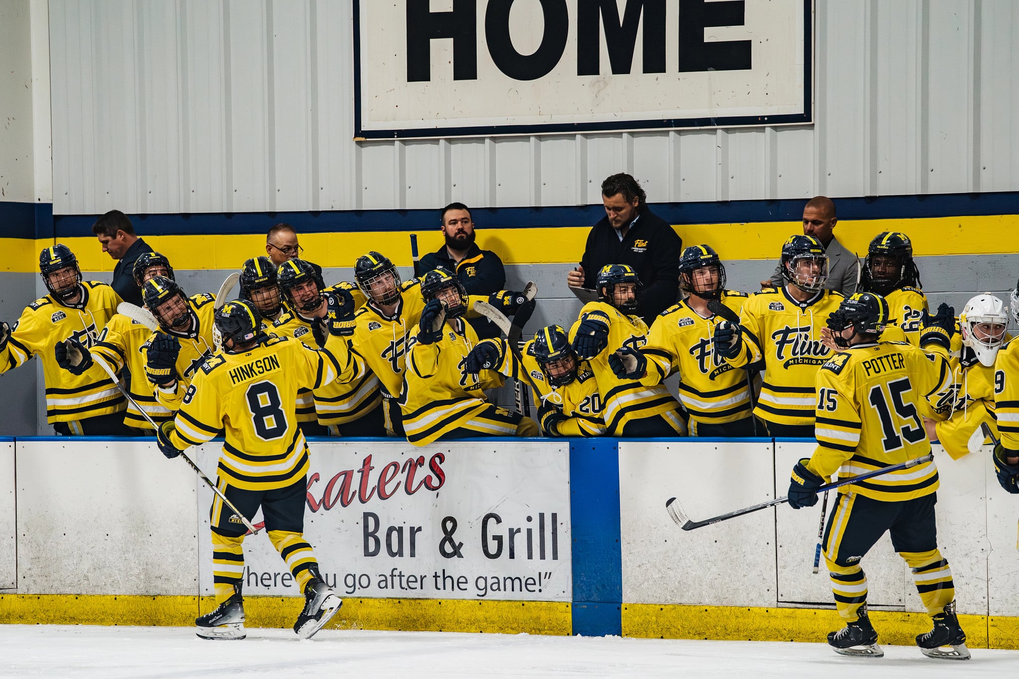 A hockey team in yellow jerseys celebrates on the bench during a game, with players and coaches engaged in the action.