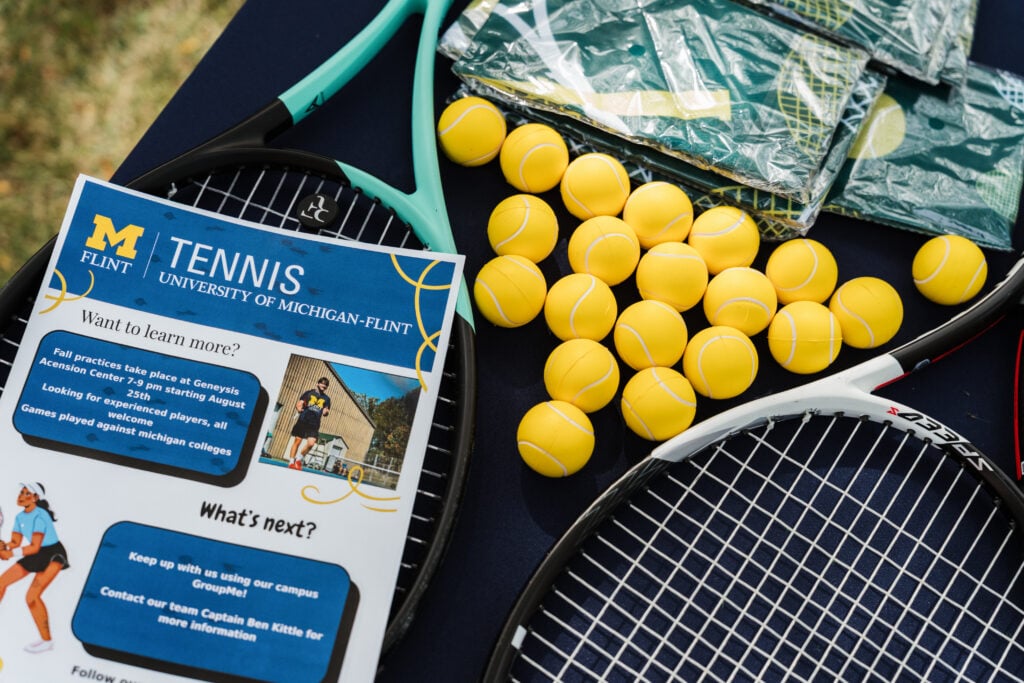 A tennis flyer for the University of Michigan-Flint is displayed alongside tennis rackets, yellow balls, and practice information.