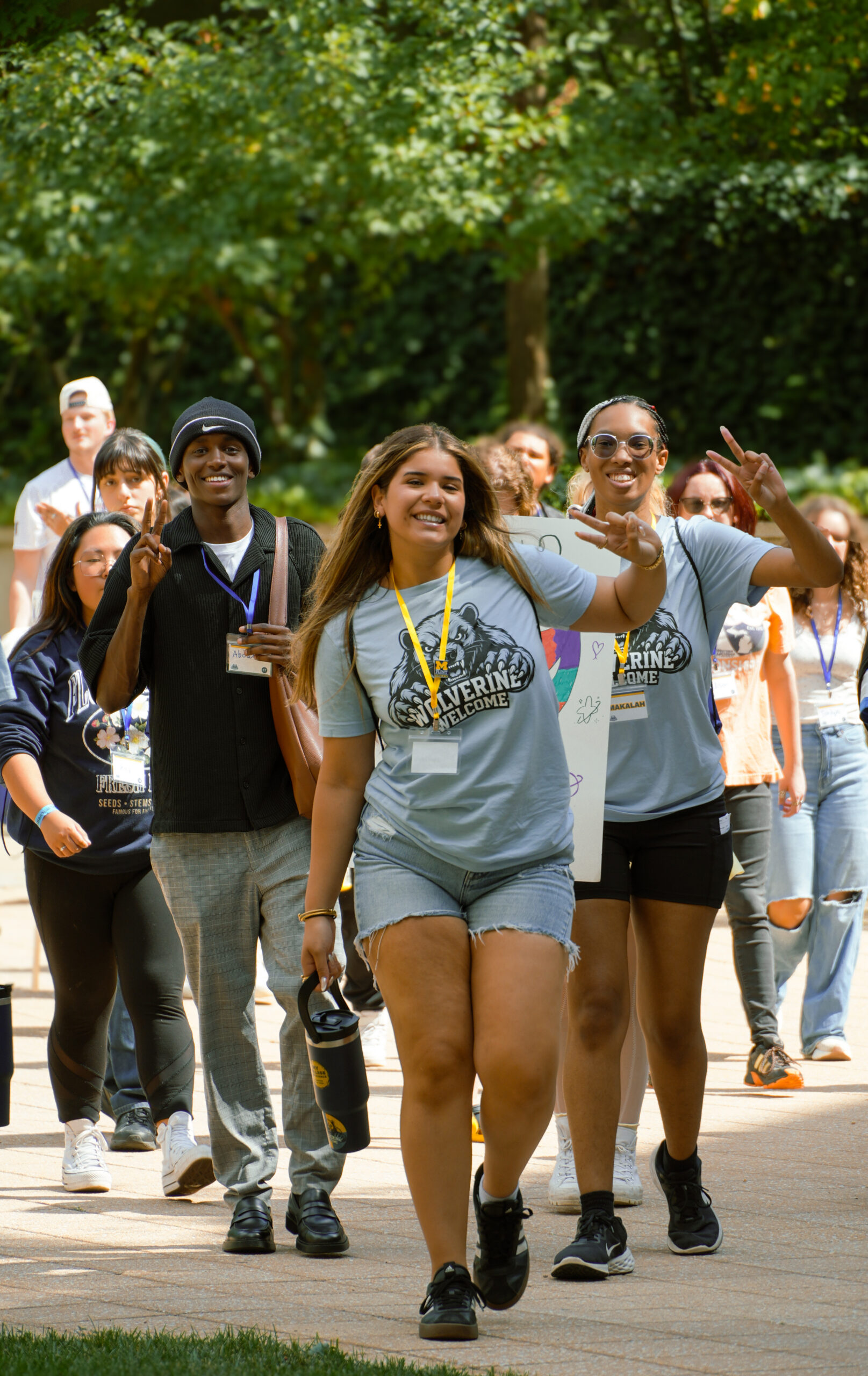 A group of people walking together outdoors, smiling and posing for the camera, with some holding signs and water bottles.