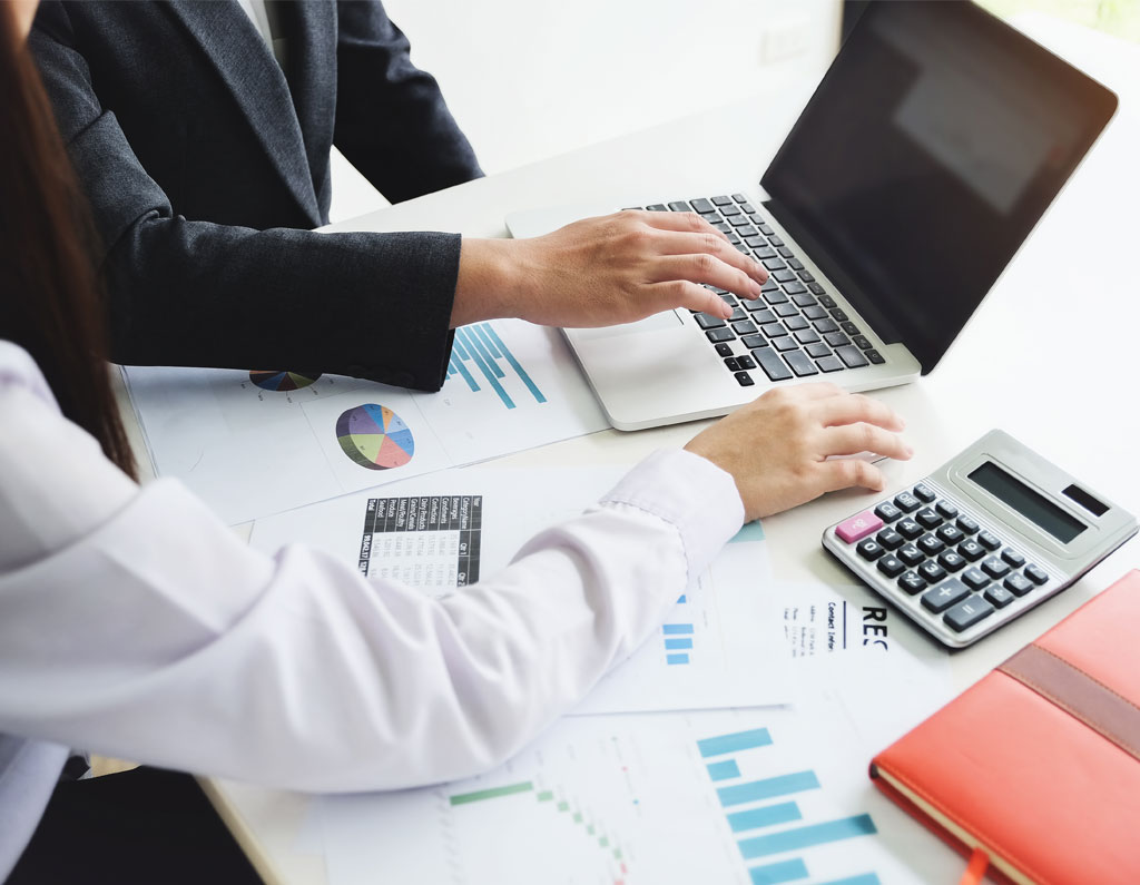 Two people are working together at a table with a laptop, financial documents, and a calculator.