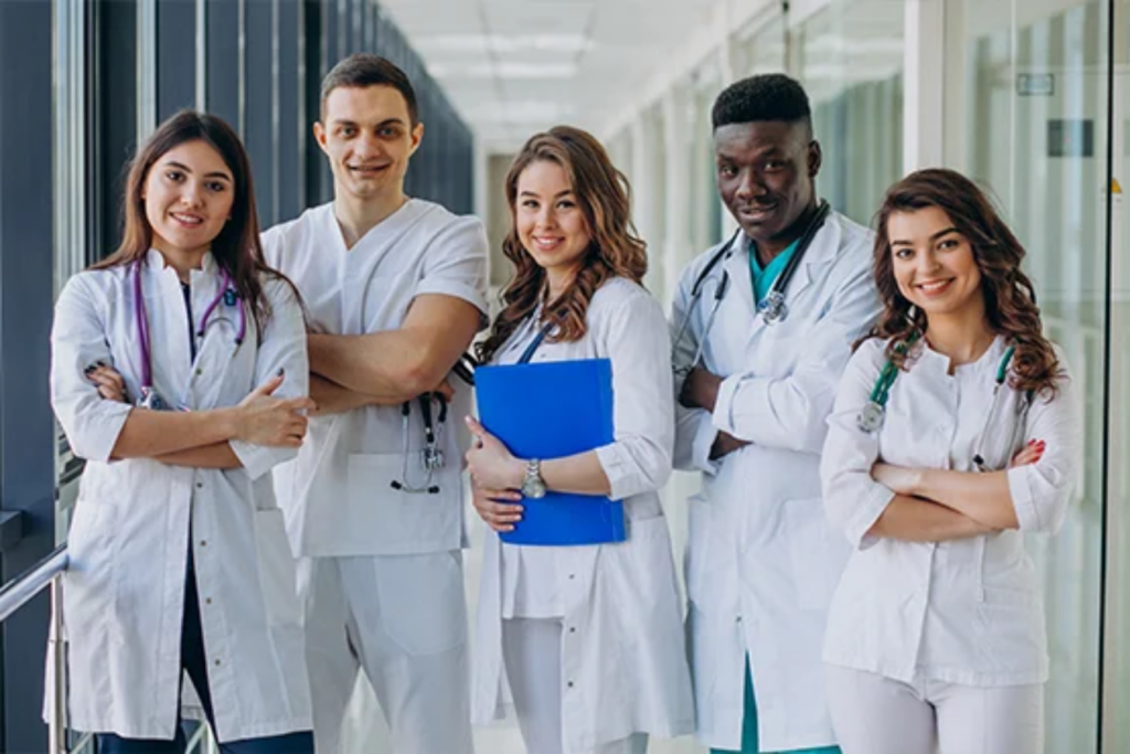 A group of five healthcare professionals in white lab coats, smiling and standing together in a hospital corridor.