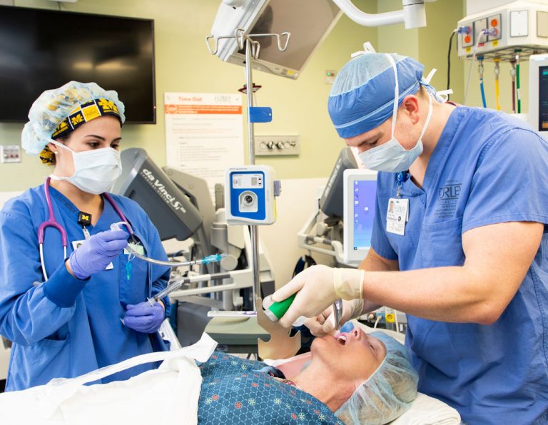 A medical team is performing a procedure on a patient in a hospital setting, with one person administering anesthesia.
