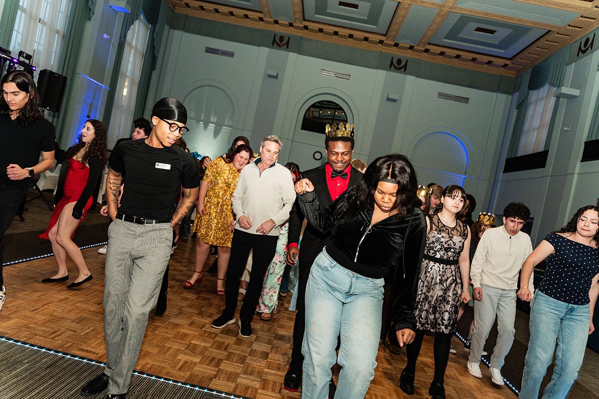 A group of people dancing together in a spacious venue, with some wearing crowns and a lively atmosphere.