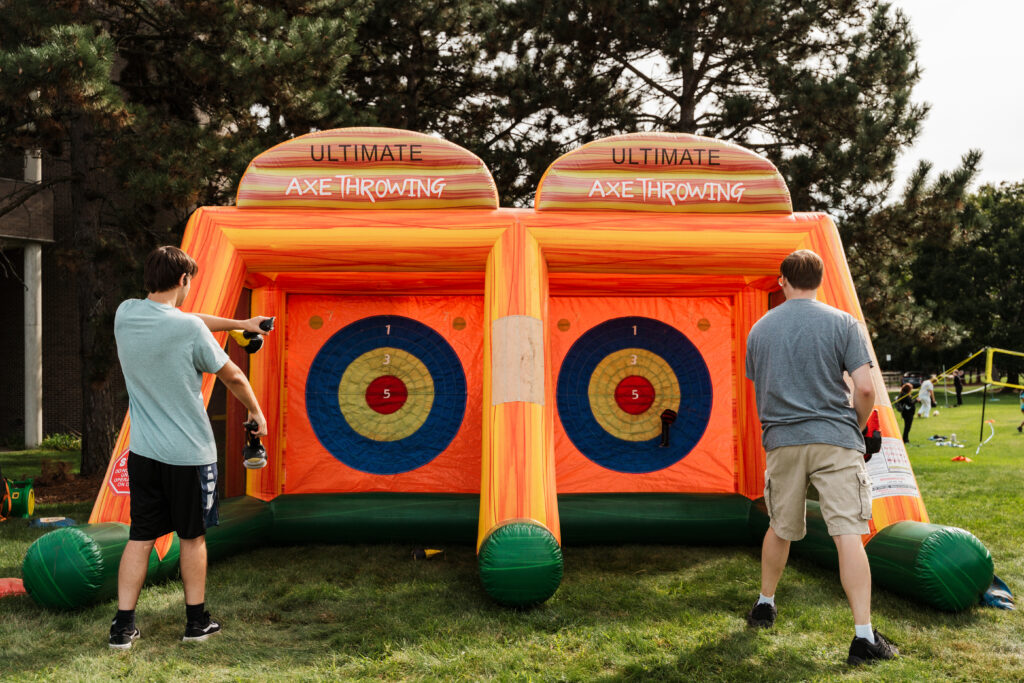Two people are participating in an inflatable axe throwing game, aiming at targets with scoring numbers.