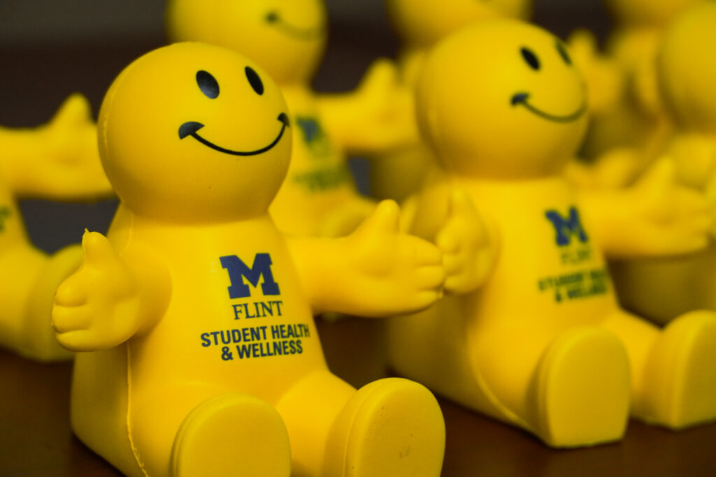 A group of yellow smiley face figurines with the text "UM FLINT STUDENT HEALTH & WELLNESS" on their bodies.