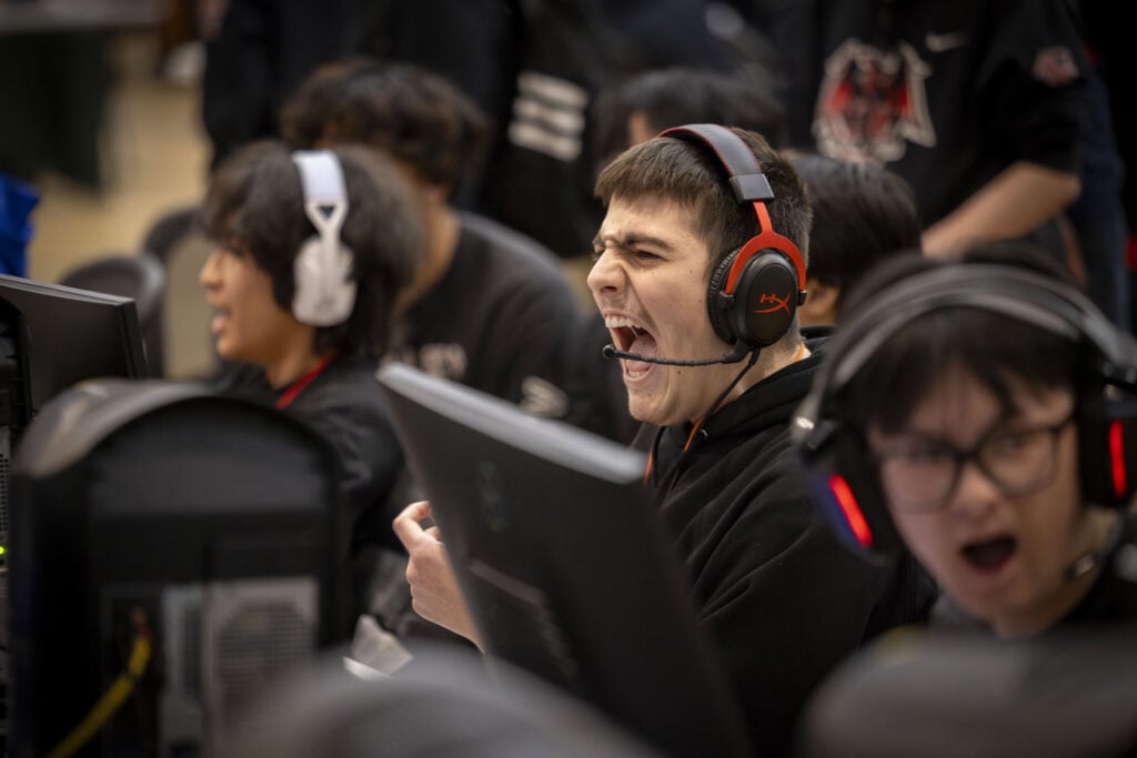 A group of gamers wearing headsets, intensely focused and cheering during a competitive gaming event.