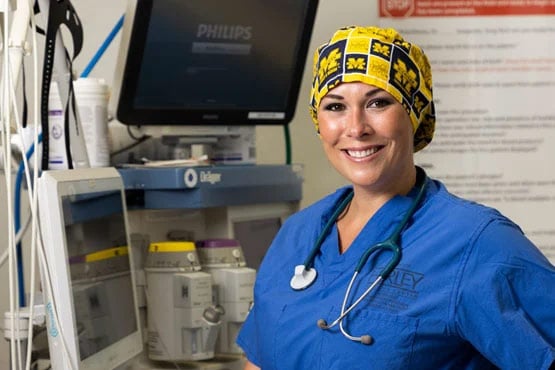 Bryanna Williams in scrubs and a patterned cap smiles while standing next to medical equipment in a healthcare setting.