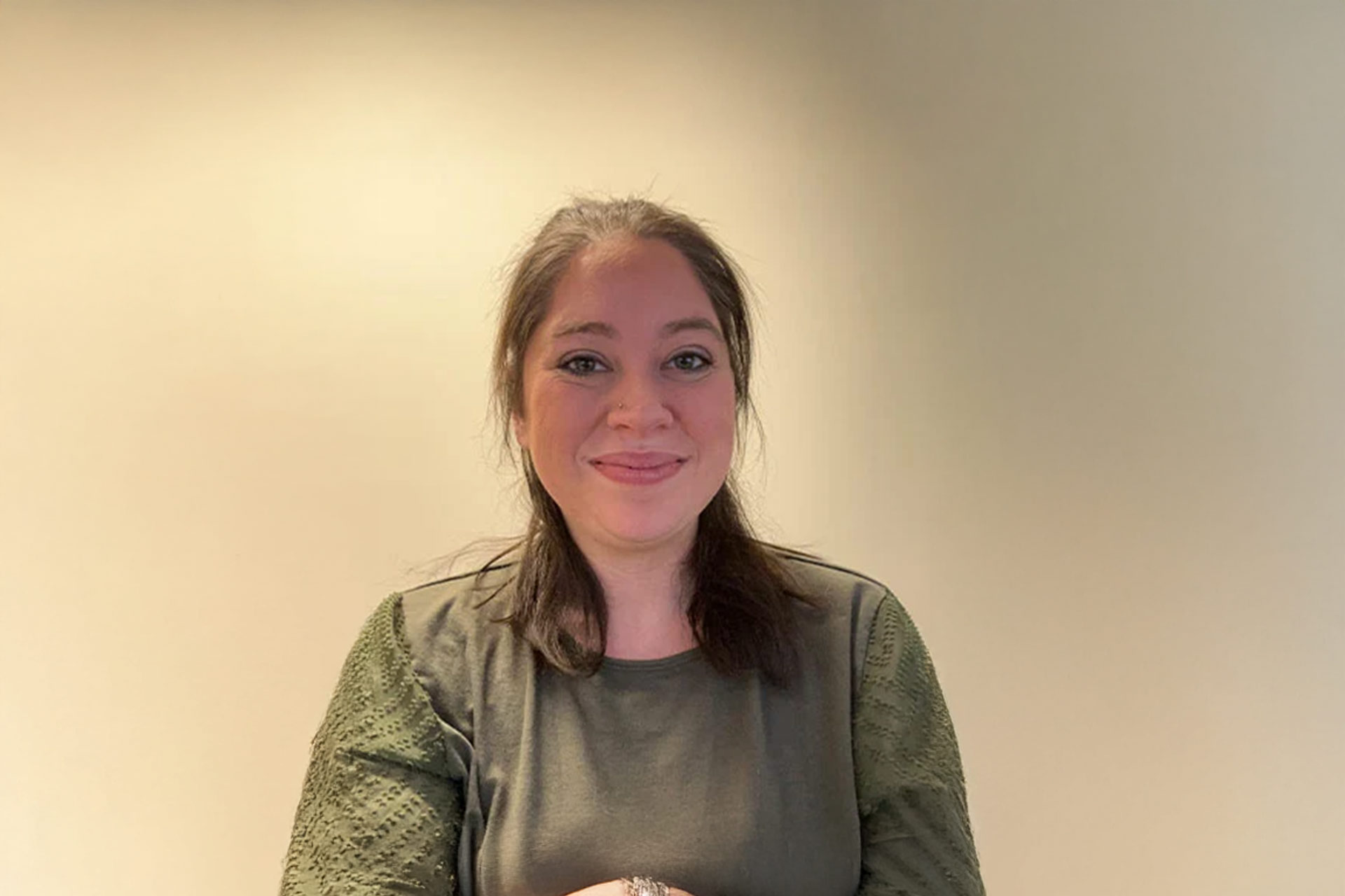 MacKenzie R. smiles while holding something in their hands, standing against a plain background.