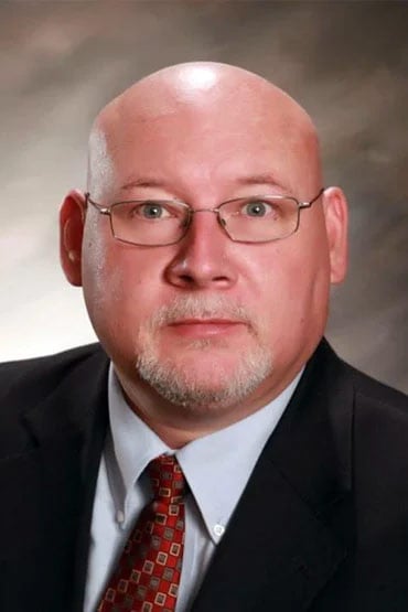 Bobby O’Steen in a suit and tie, wearing glasses, poses for a professional headshot against a neutral background.