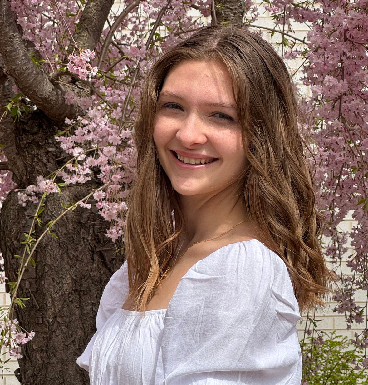 Kaitlyn G. smiles while standing near a tree with pink blossoms.