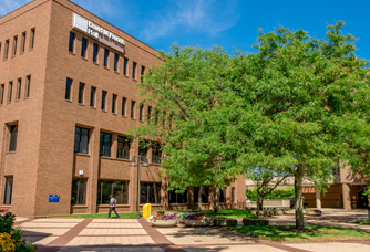 Exterior of French Hall, a brick building on the UM-Flint campus, with a tree-lined walkway.