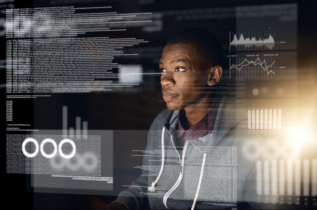 A person sits in front of a computer, surrounded by digital data and graphs displayed on screens.