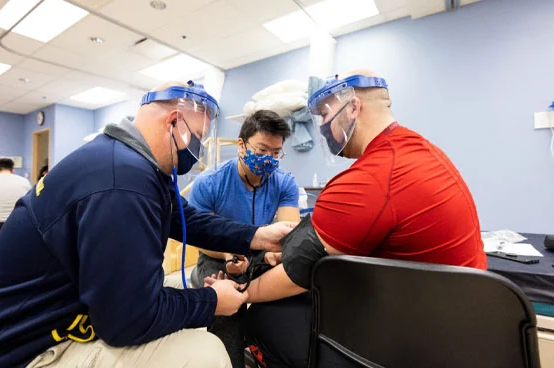 Two people are assisting another person in taking a blood pressure reading in a medical setting.