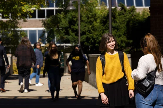 A group of people walking on a sunny day in an outdoor setting, with one person in a yellow sweater in the foreground.