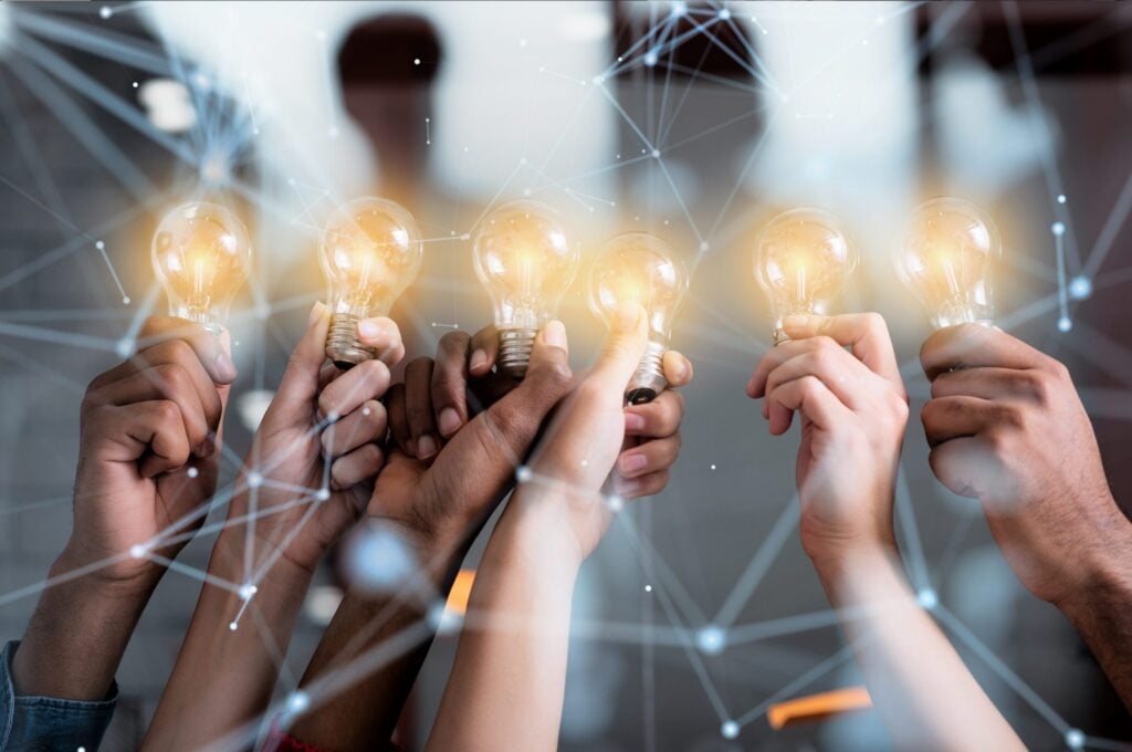 A group of hands holding light bulbs, symbolizing ideas and innovation, against a blurred background with a network design.