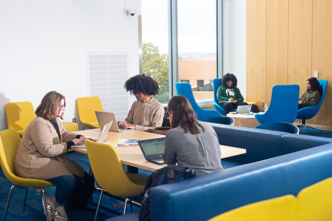 Students studying together at tables in a campus lounge.