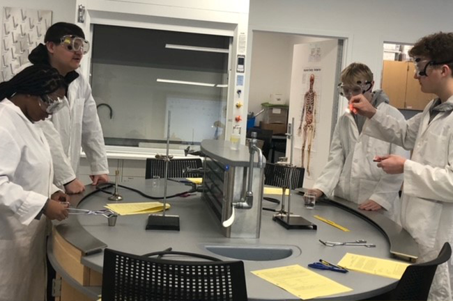 Students in lab coats and safety goggles conducting a chemistry experiment.